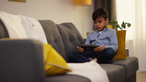 Young-Boy-Sitting-On-Sofa-At-Home-Playing-Game-Or-Streaming-Onto-Handheld-Gaming-Device-6